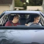 A man sitting in his car and making a concerned face, looking worried, suggesting engine problems.