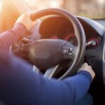 Hand on a steering wheel of a car indicating potential engine issues